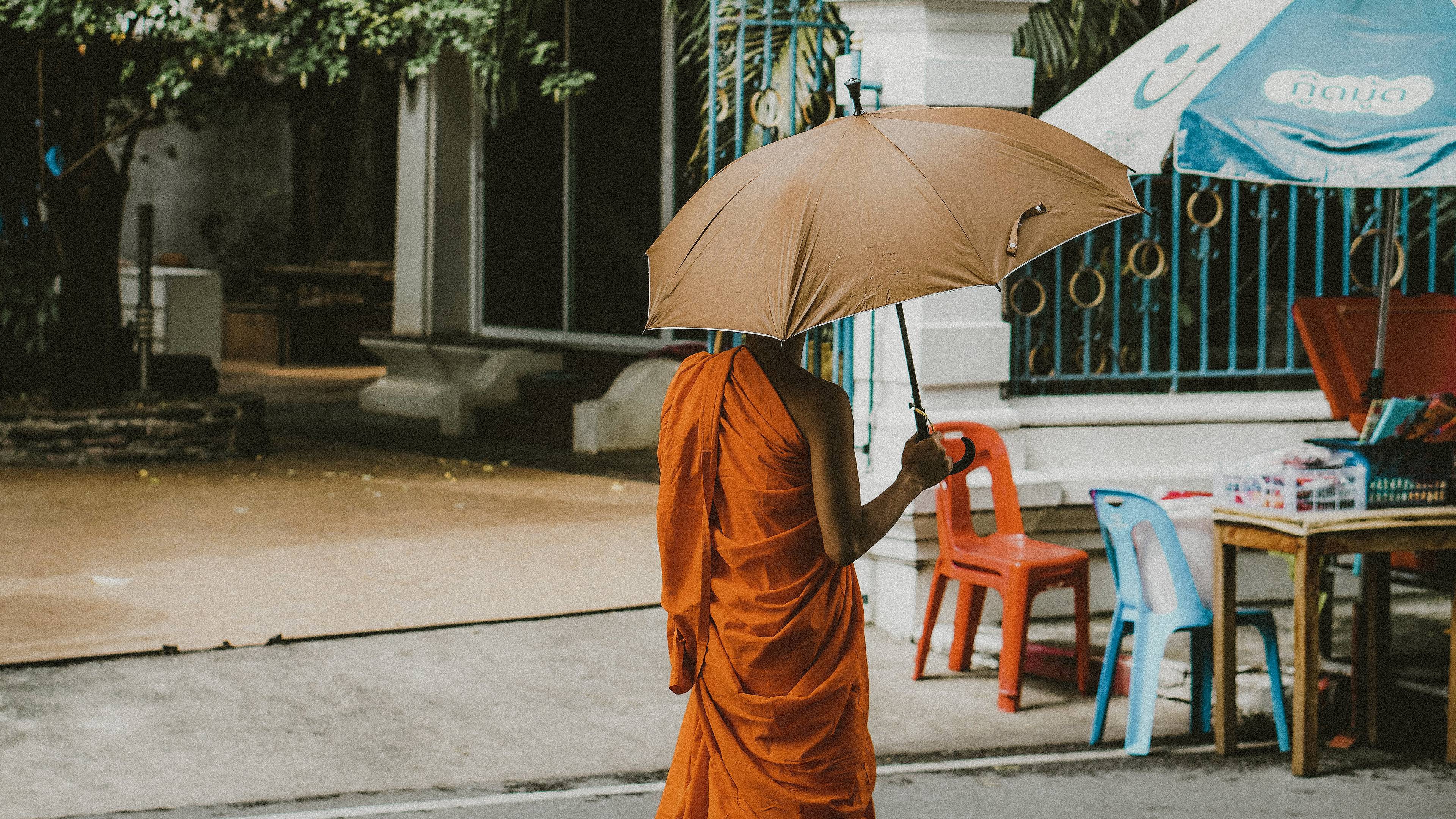 Mönch geht unter einem Regenschirm eine Straße entlang