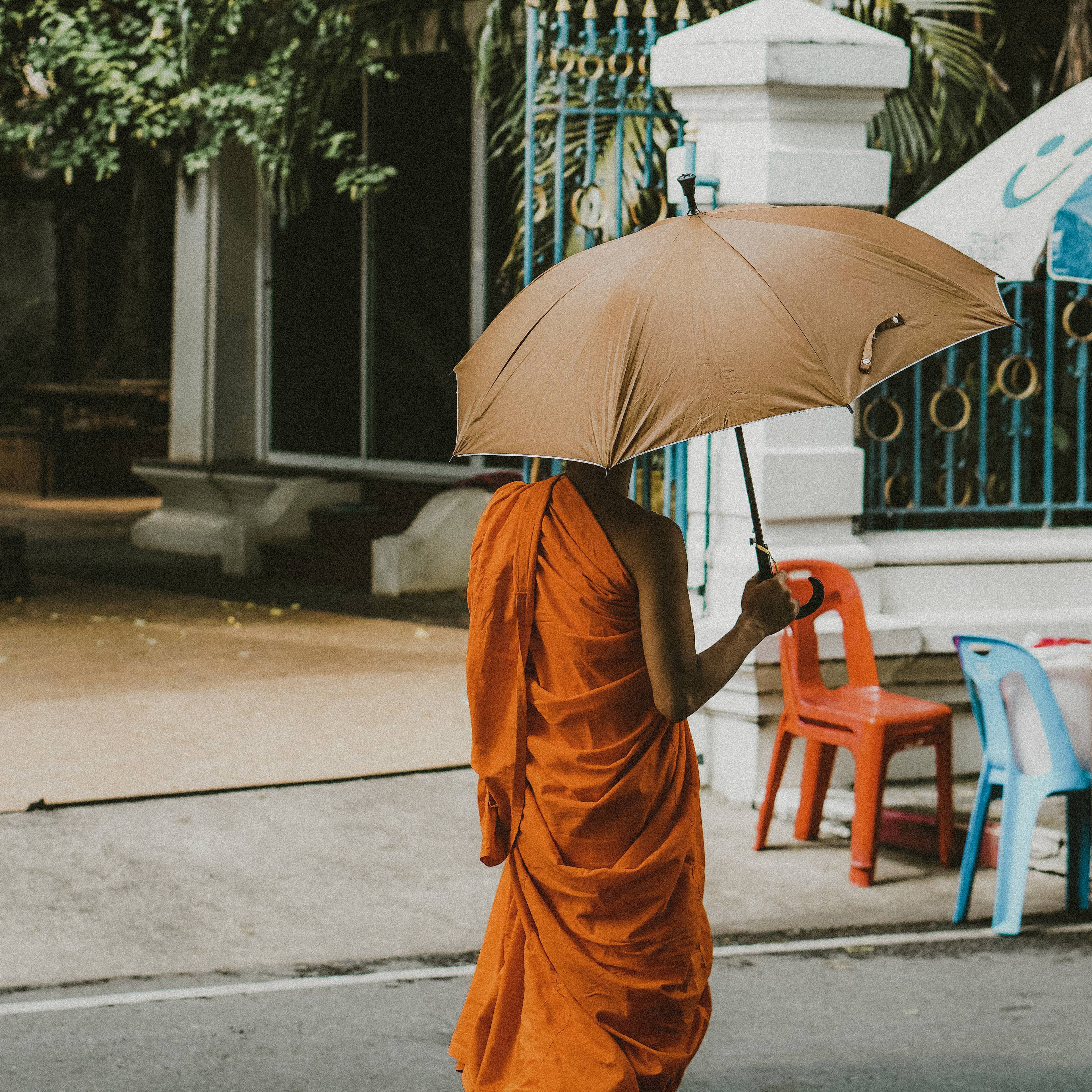 Mönch geht unter einem Regenschirm eine Straße entlang